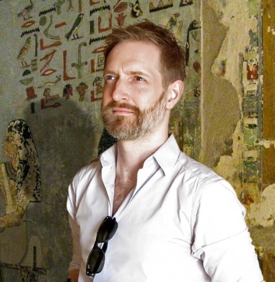 A person standing in front of an ancient Egyptian wall with hieroglyphics and artwork.